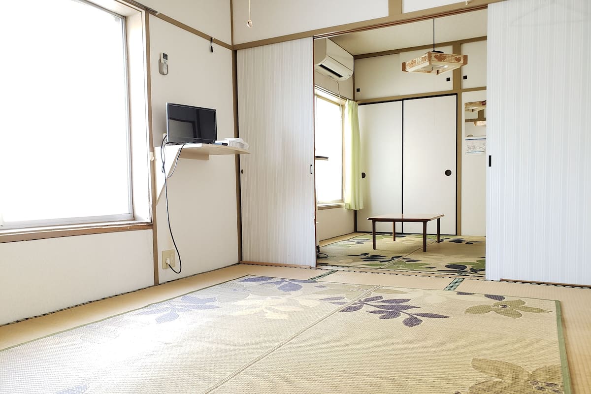 A traditional Japanese room with tatami flooring, a tatami mat with a floral pattern, a low table, and sliding doors.