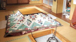 Een traditionele Japanse kamer met tatami vloeren, een futon bed, een shoji schuimeldeur en een houten plafond met een decoratieve ventilator.