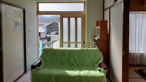 Een kamer met een groene sofa met patroon, een houten kast en een schuifdeur naar een balkon.