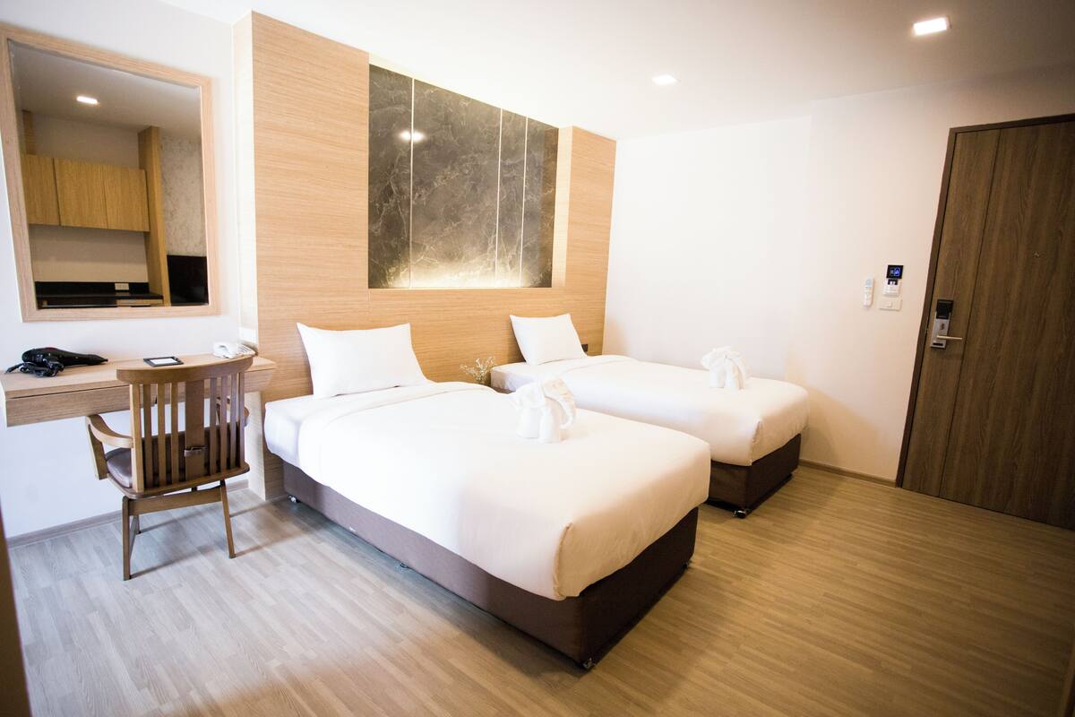 Une chambre d’hôtel avec deux lits, un bureau, une chaise et un miroir.