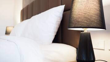 A neatly made bed with white linens, a black textured lamp on a wooden nightstand, and a brown headboard.