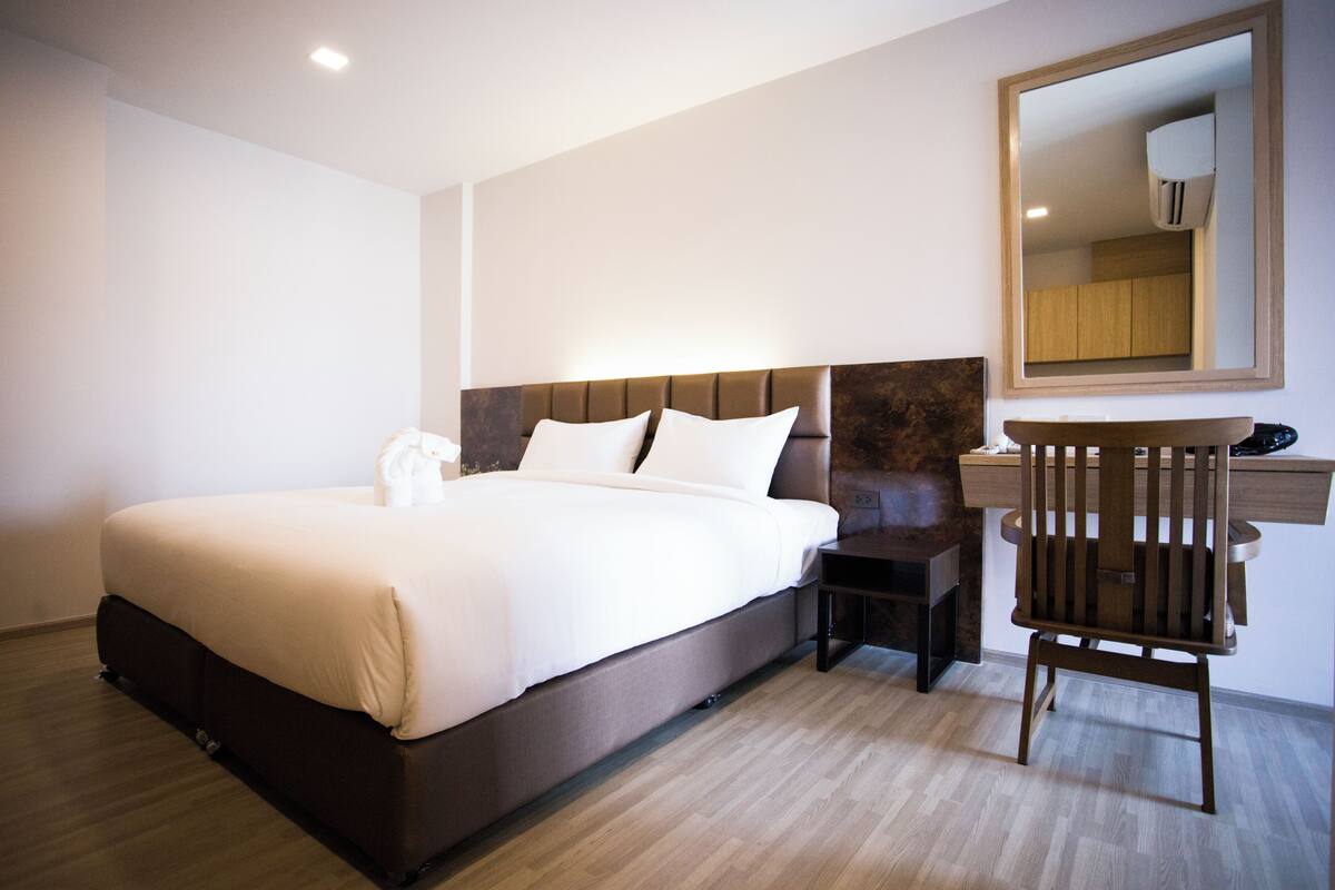 Une chambre d’hôtel moderne avec un grand lit, une table de chevet, une chaise et un miroir au mur.