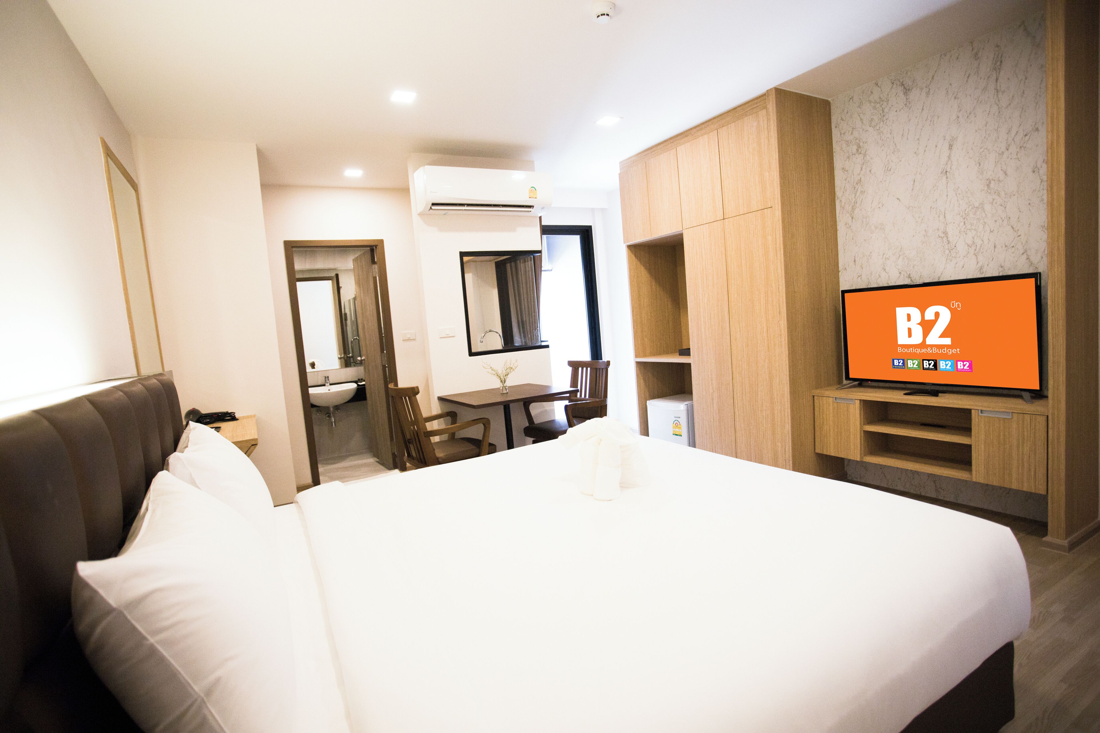 A hotel room with a large bed, a desk with a chair, a television, and a bathroom visible through an open door.
