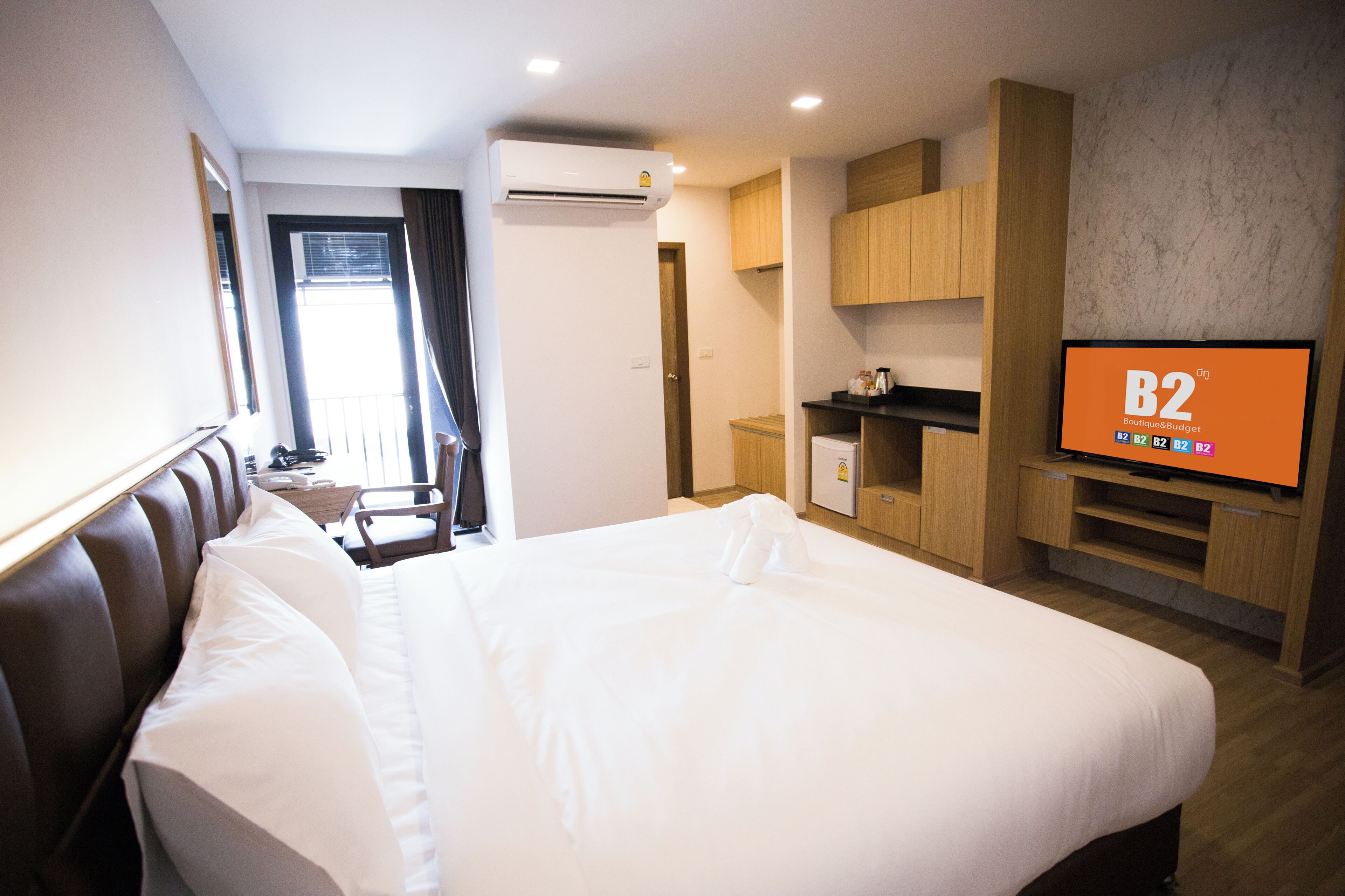 A hotel room with a large bed, a TV displaying 'B2 Boutique Budget', a desk, and a wardrobe.