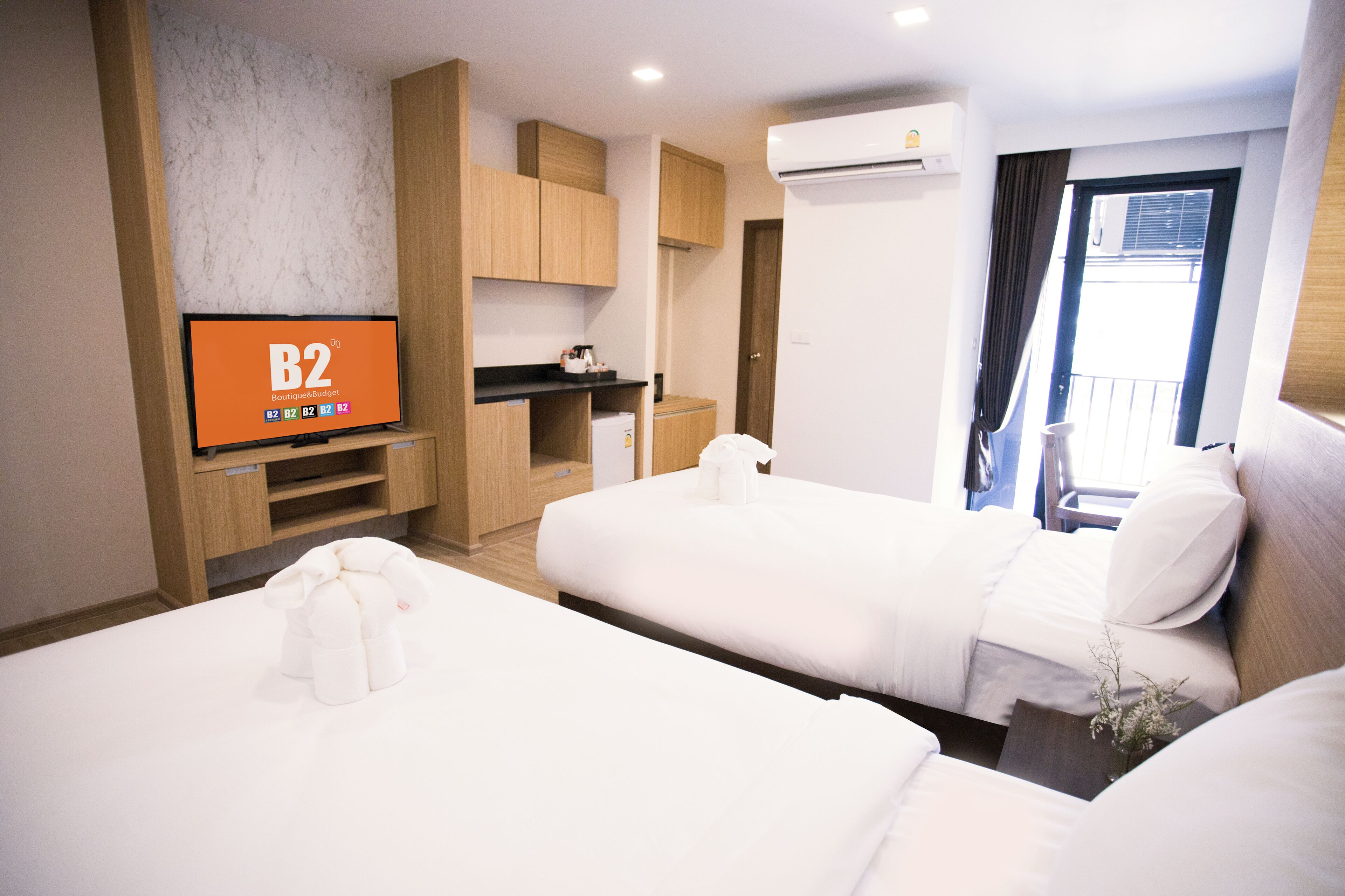 Une chambre d’hôtel avec deux lits, un téléviseur diffusant « B2 Boutiqueblogspot », une kitchenette et un balcon avec vue.