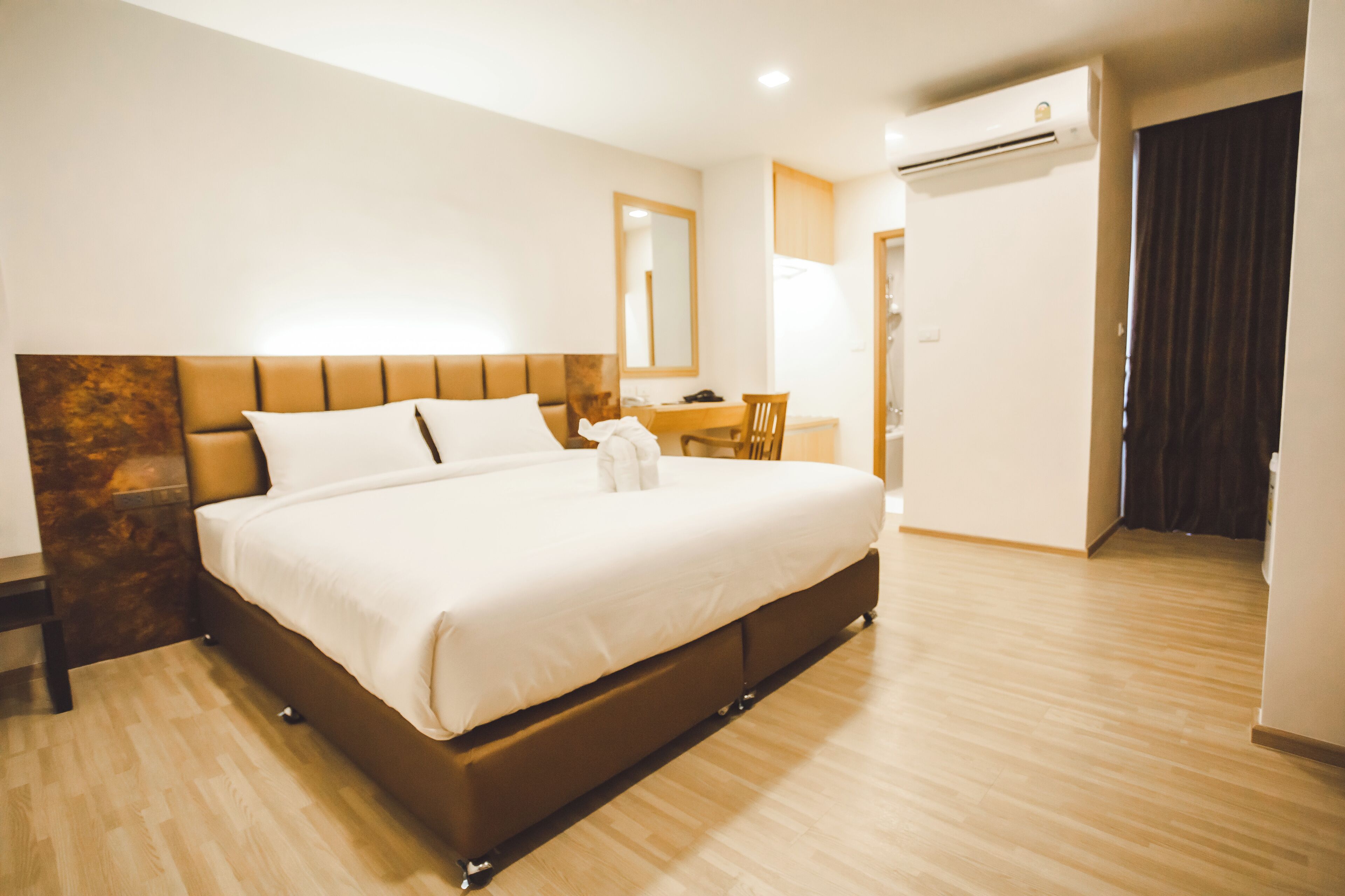 A hotel room with a large bed, a desk, a chair, and an air conditioning unit.