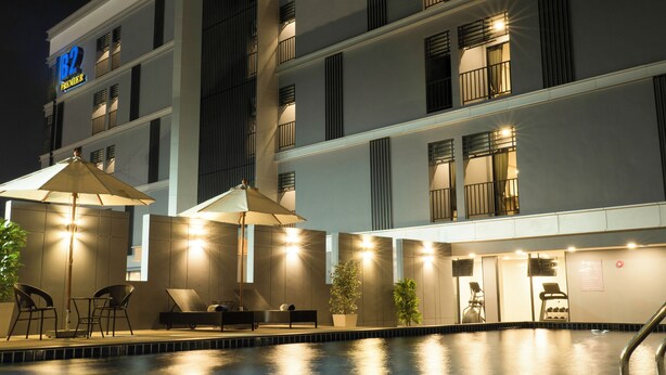 Une vue de l’extérieur d’un hôtel de nuit, avec une piscine, des espaces de détente en plein air et une enseigne indiquant « B2 Premier ».