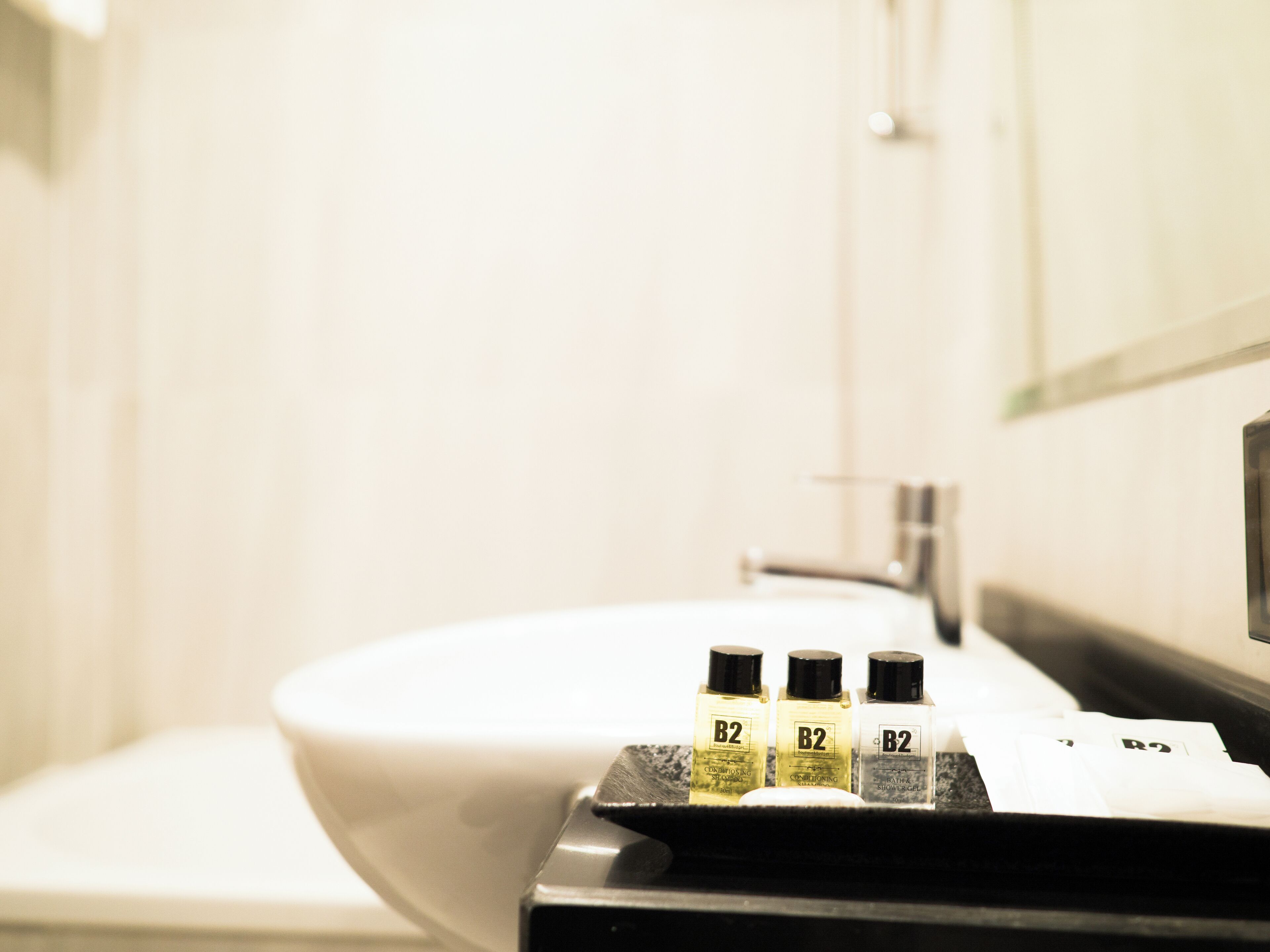 Un baño con un lavamanos blanco, tres botellas de champú acondicionador B2 y una bandeja negra.