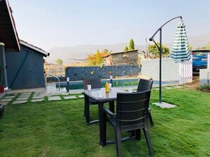 A backyard with a table and chairs, a small pool, and a stone wall. - Spicy Mango Malhotra's Pristine Villa (Karjat)