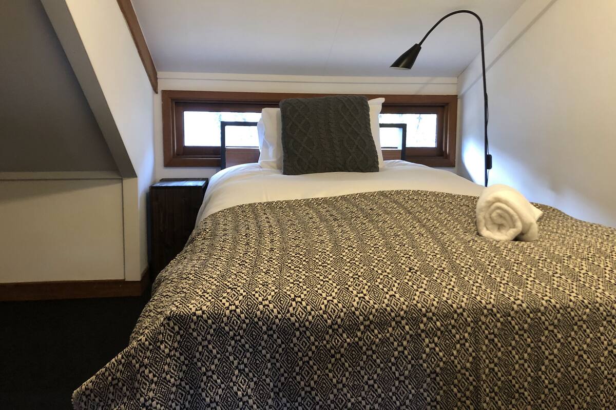 A neatly made bed with a patterned blanket, a rolled towel, and a lamp on the side.