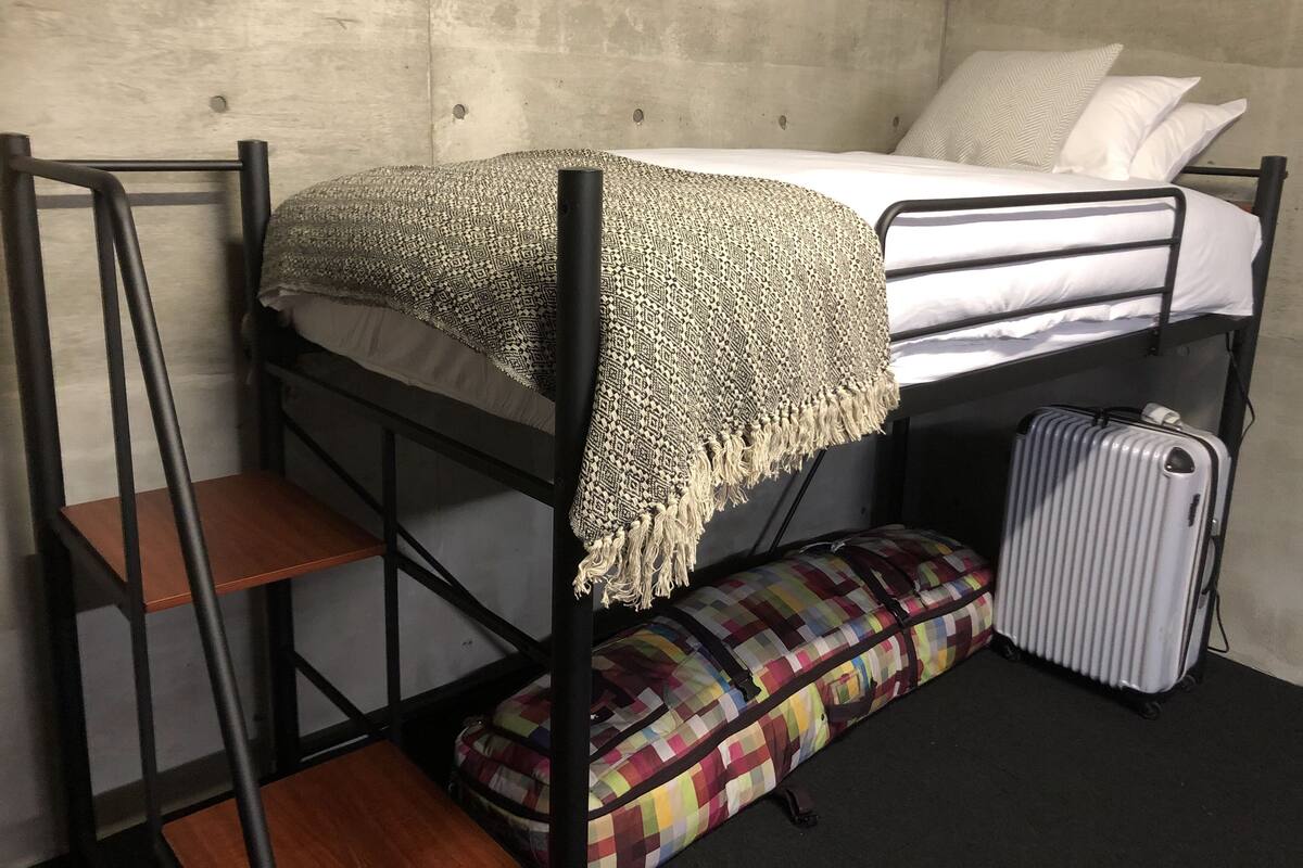 A bunk bed with a patterned blanket, a suitcase, and a colorful bag.