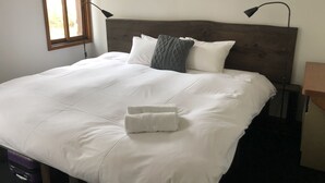 En pænt redt seng med hvide sengetøj og et foldet håndklæde, et træsengegærde og to sengeborde med lamper.