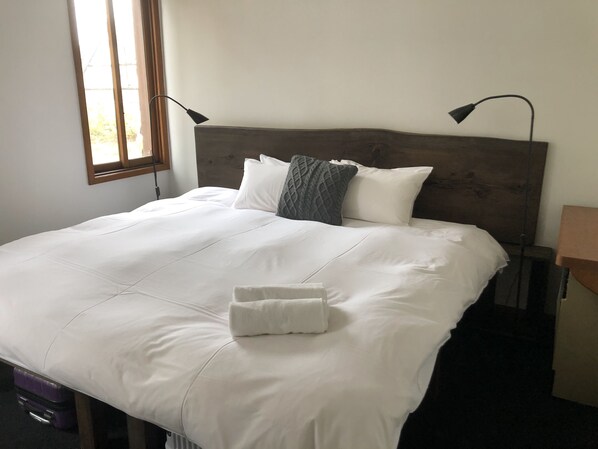 A neatly made bed with white linens and a folded towel, a wooden headboard, and two bedside lamps.