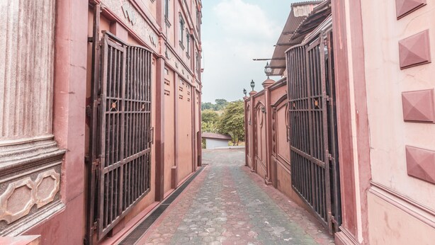A narrow alleyway between pink buildings with large metal gates and a cobblestone path. - Super OYO 1640 Fallinda Hotel (Cibinong)