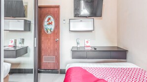 A hotel room with a bed, a wooden door, a TV mounted on the wall, a small desk with a mirror, and a shelf above the desk. - Super OYO 1640 Fallinda Hotel (Cibinong)