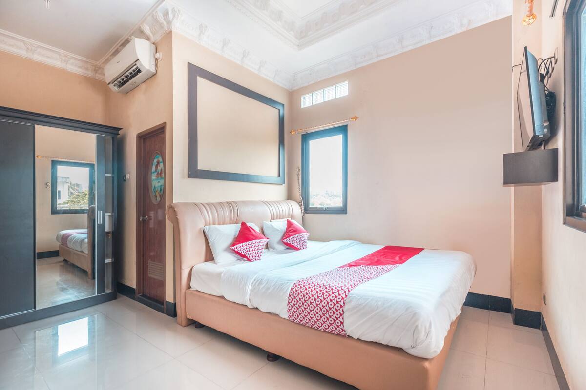 Une chambre d’hôtel avec un lit, une armoire, un miroir et une fenêtre.