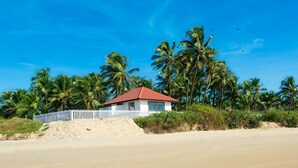 A beachfront property with a white house, palm trees, and a sandy beach.