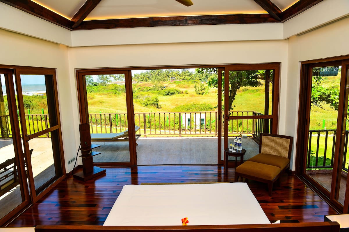 Una habitación con una cama grande, piso de madera y un balcón con vistas a un área verde y árboles.