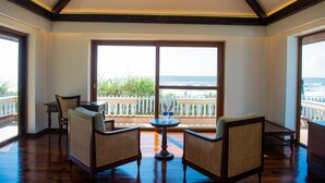 A room with a large window overlooking the ocean, furnished with wicker chairs and a small table.