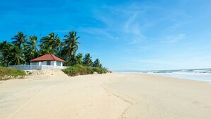 A beach with a small building, palm trees, and the ocean.