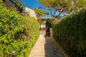 A stone pathway leading to a building with a tiled roof and a black gate. - Villa Es Clot sea view 8 people BBQ (Alcúdia)