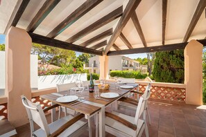 A covered outdoor dining area with a table set for four, surrounded by white chairs.