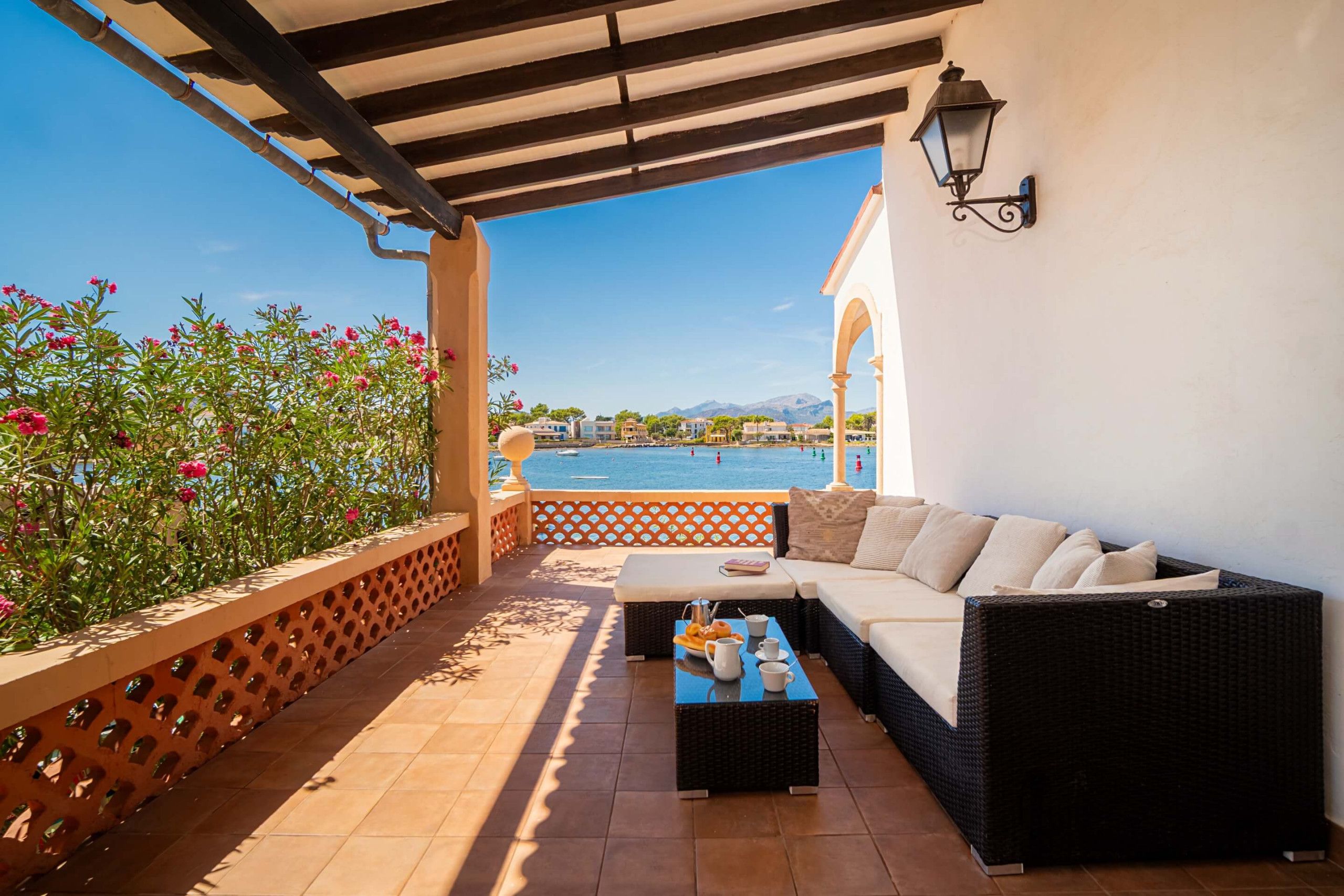 Eine Terrasse mit einer Couch, einem Tisch mit Frühstücksangebot und Blick auf das Meer, sowie ein Pergola.