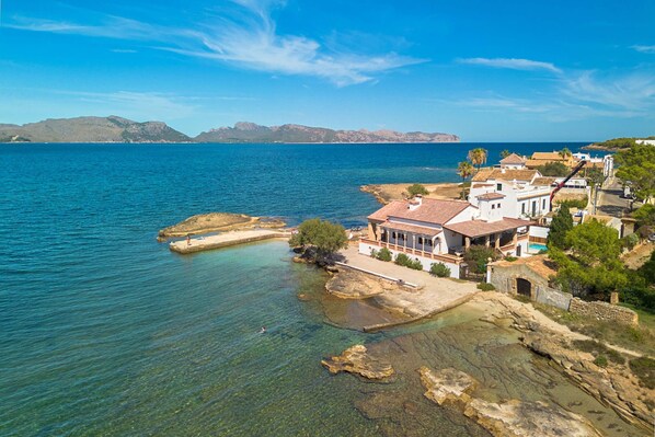 A coastal property with clear waters, rocky shoreline, and a view of distant mountains.