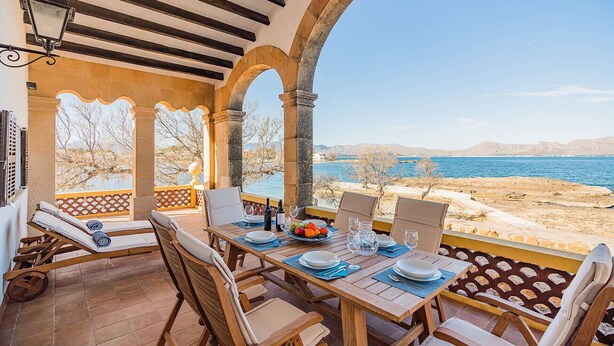 A terrace with wooden furniture, a table set for dining, and a view of the sea and mountains.