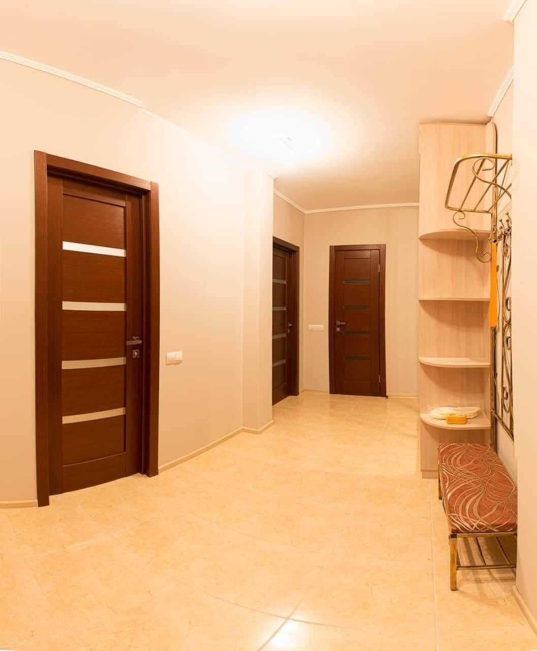 A hallway with two wooden doors, a bench, and a metal shelf unit.