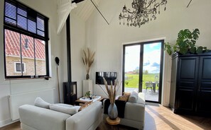 Un salón moderno con sofá, una mesita, televisión y chimenea. Se ve un jardín a través de una puerta corredera.