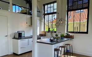 Cocina moderna con una isla central, taburetes de bar y vistas a un edificio de ladrillo.