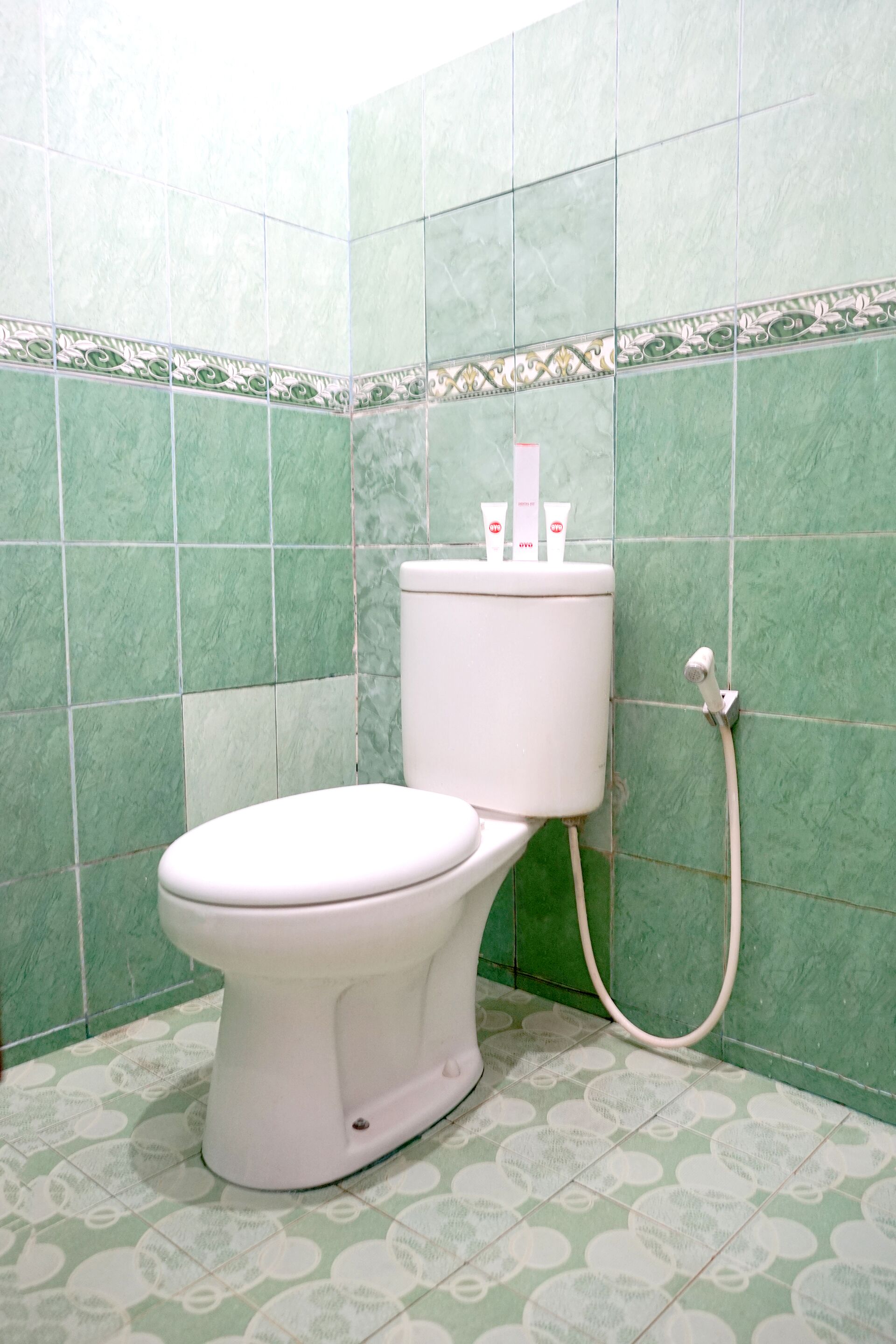 Un inodoro en un baño con azulejos verdes y piso estampado.