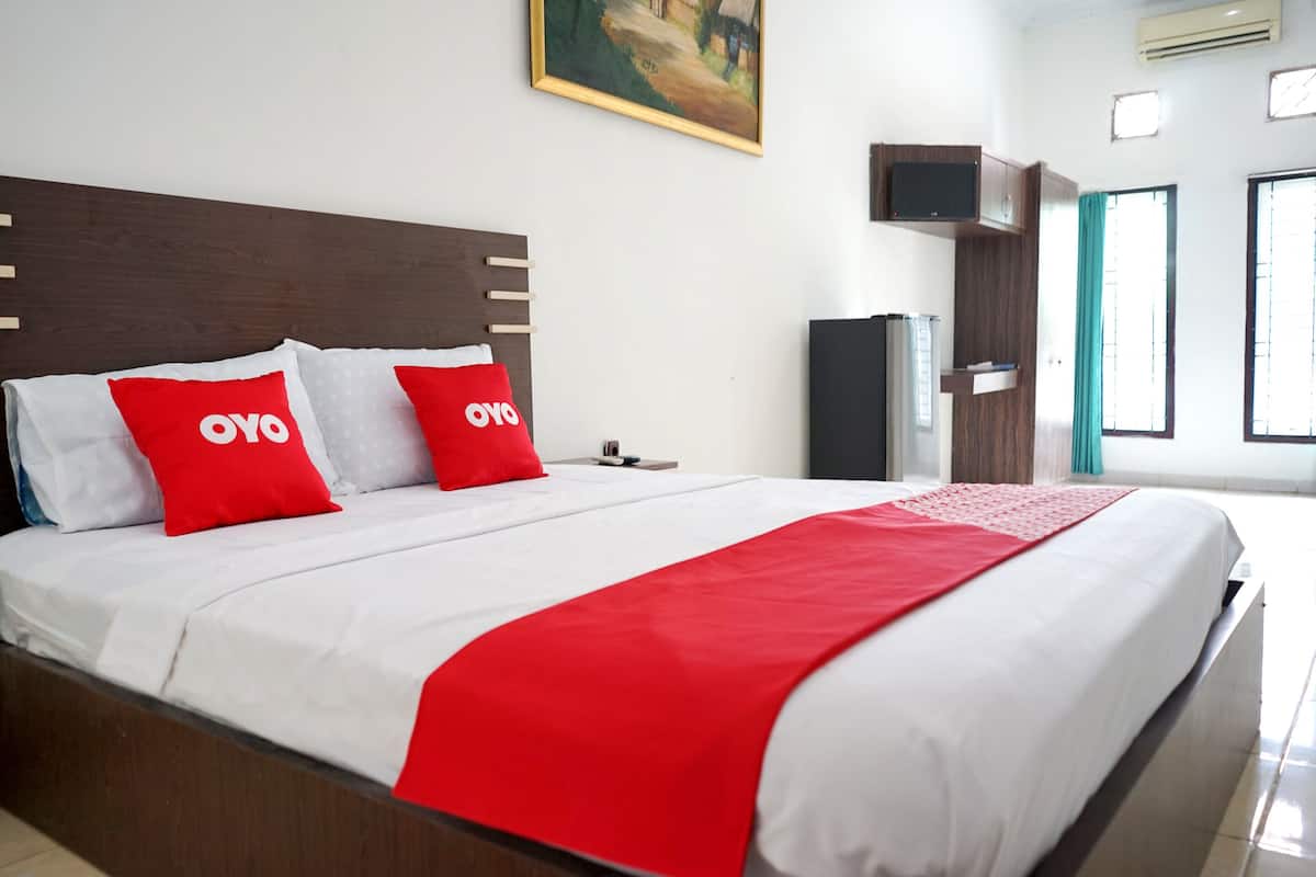Una cama bien hecha con ropa de cama roja y blanca, un cabecero de madera y una manta roja.