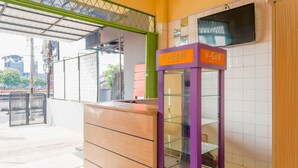 A reception area with a wooden counter, a purple V-Gen information kiosk, and a tiled wall with a TV. - OYO 1850 The Trend (Jakarta)