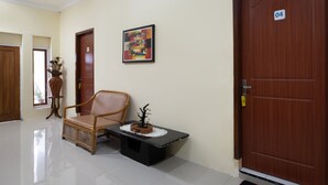 A hallway with a wooden door labeled '04', a framed abstract painting, a wicker chair, and a small table with a plant. - Hotel O Bromo Hill (Sukapura)