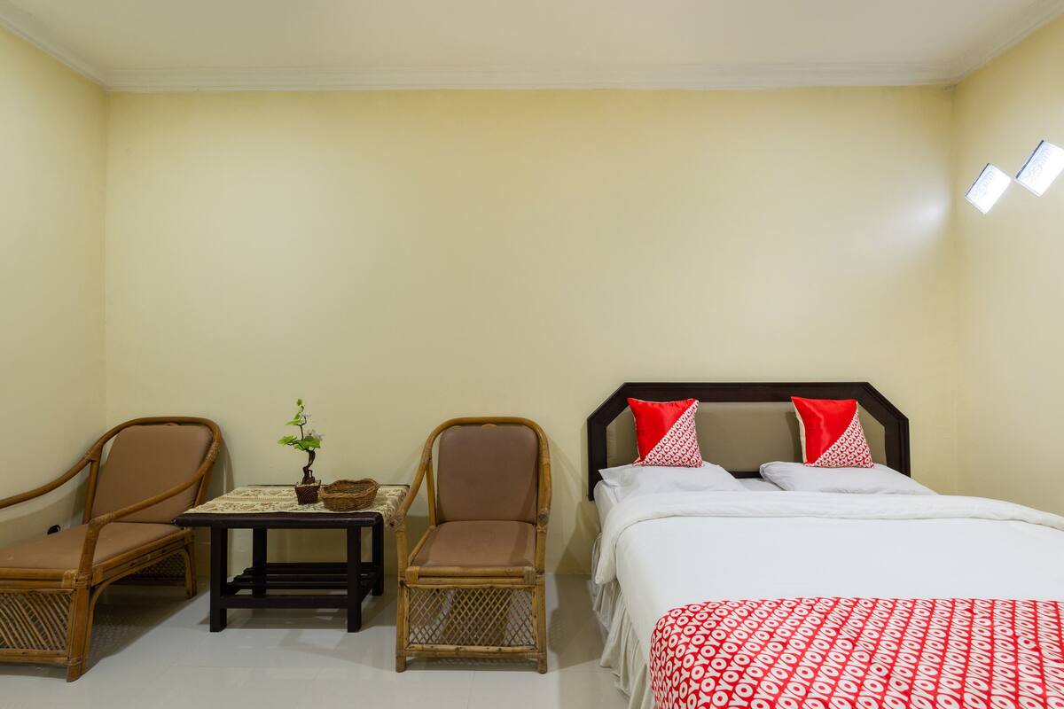 Ein Hotelzimmer mit einem Bett, zwei Korbstühlen, einem kleinen Tisch mit Pflanze und einem Nachttisch.