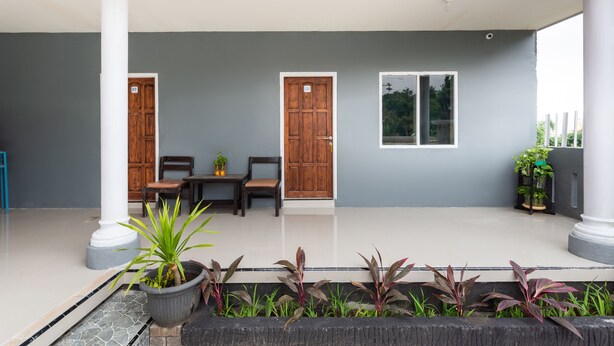 A covered outdoor area with two wooden doors, a table with chairs, and potted plants. - Hotel O Bromo Hill (Sukapura)