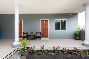 A covered outdoor area with two wooden doors, a table with chairs, and potted plants. - Hotel O Bromo Hill (Sukapura)