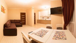 A living room with a sofa, a dining table with two placemats, a TV mounted on the wall, and a kitchen area with cabinets and a countertop. - Apart Kiev Kopernika 3-2 (Kyiv)