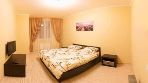 A hotel room with a bed, a TV on a stand, a nightstand, and a picture on the wall. - Apart Kiev Kopernika 3-2 (Kyiv)