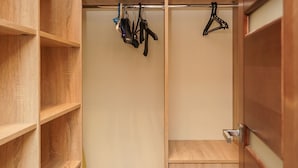 Un placard en bois doté de plusieurs étagères et d’un espace pour suspendre des vêtements, avec une porte coulissante et un sol carrelé.