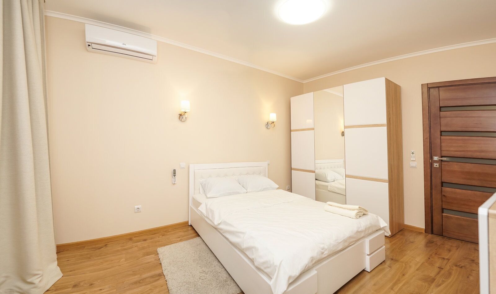 A bedroom with a bed, a wardrobe, a mirror, a door, and an air conditioning unit.