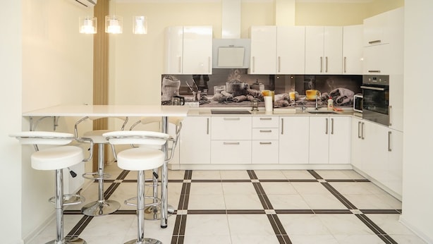 Une cuisine moderne avec des meubles blancs, un îlot central doté de tabourets de bar et un sol carrelé avec un motif noir et blanc.