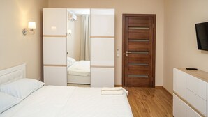 Une chambre d’hôtel avec un lit, une armoire, un miroir, une télévision et une salle de bain visible à travers une porte ouverte.