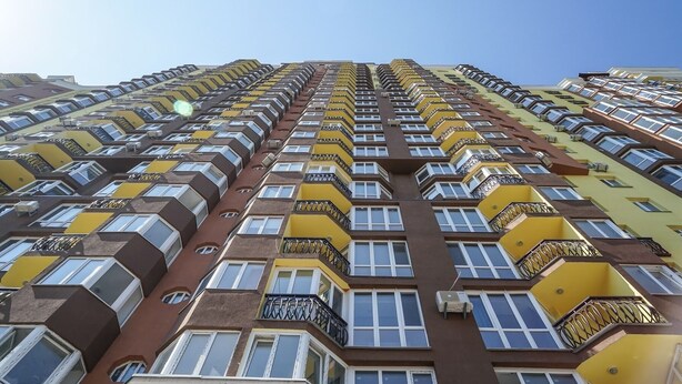 Un immeuble résidentiel de grande hauteur doté de nombreux balcons, chacun ayant une petite fenêtre et une rambarde en métal.