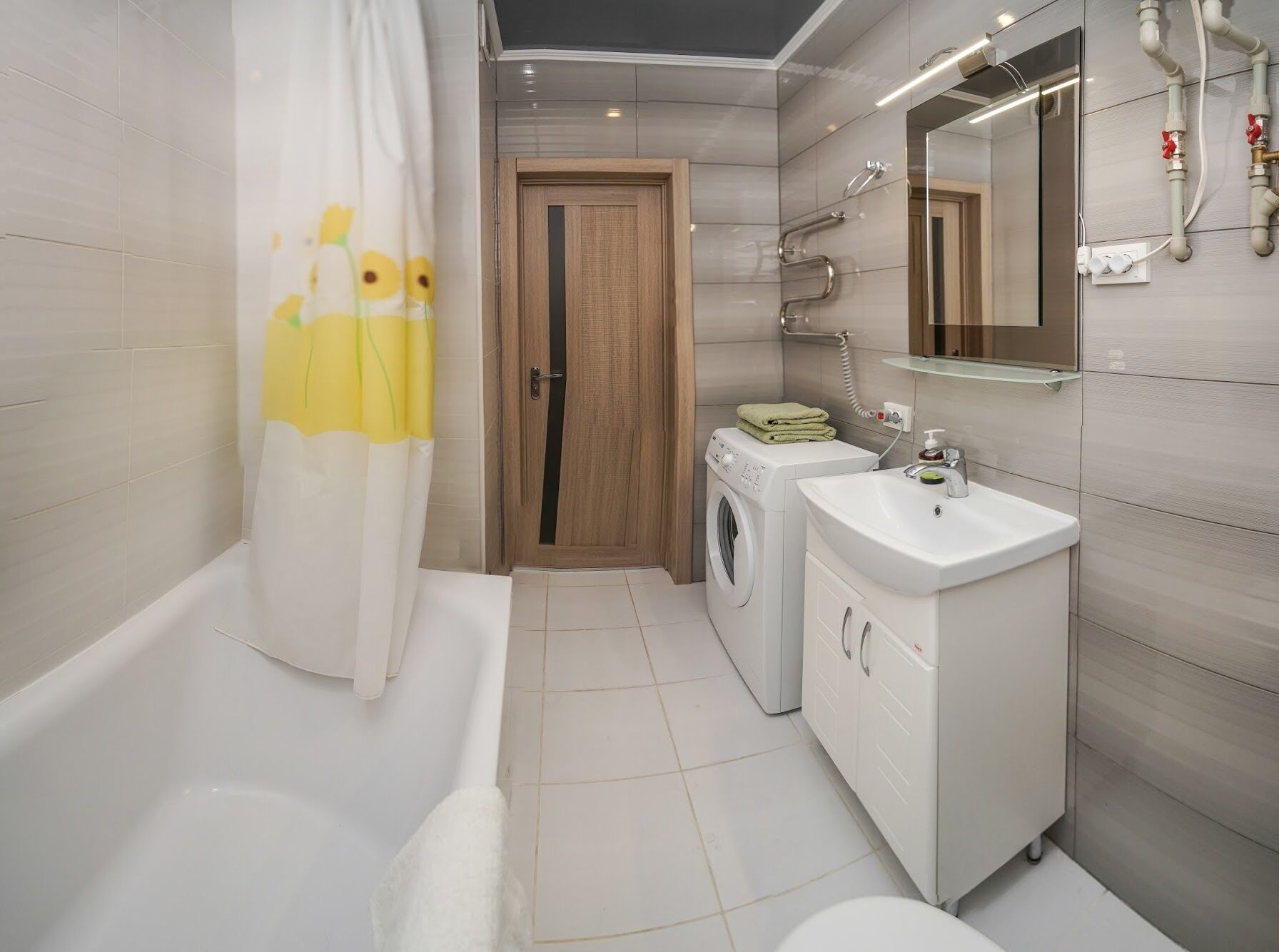 A modern bathroom with a bathtub, a washing machine, a sink, and a mirror.
