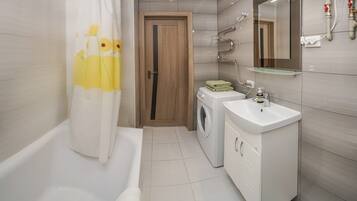 A modern bathroom with a bathtub, a washing machine, a sink, and a mirror.
