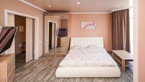 Une chambre à coucher comprenant un lit, une télévision, un miroir, une commode en bois et un banc.