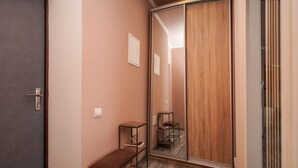 Un couloir avec une porte coulissante, un banc, une petite table et un miroir qui reflète la porte.